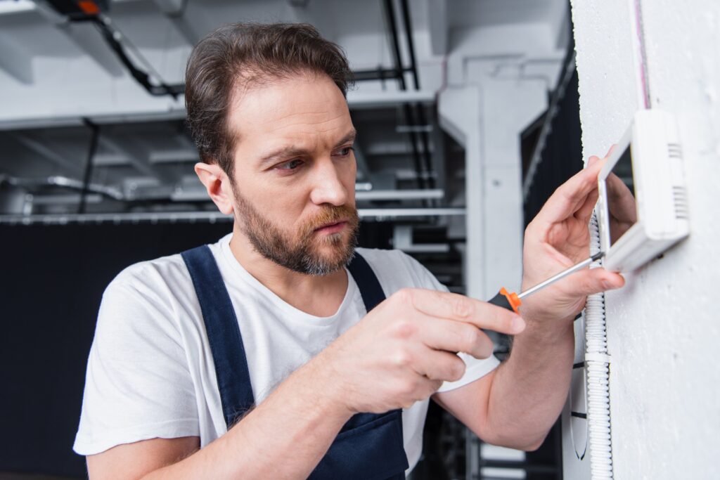 adult male craftsman fixing electrical panel by screwdriver